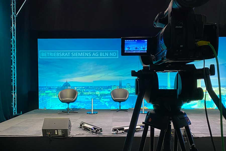Kamera zeigt auf drei Sessel auf einer Bühne